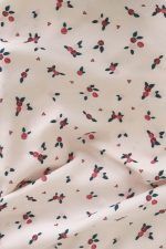 Tela de color blanco crema, con estampado de ramilletes de flores pequeñas en tonos rojos y rosas con hojas verdes, se encuentra sobre un mantel de esparto.