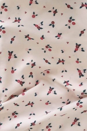 Tela de color blanco crema, con estampado de ramilletes de flores pequeñas en tonos rojos y rosas con hojas verdes, se encuentra sobre un mantel de esparto.