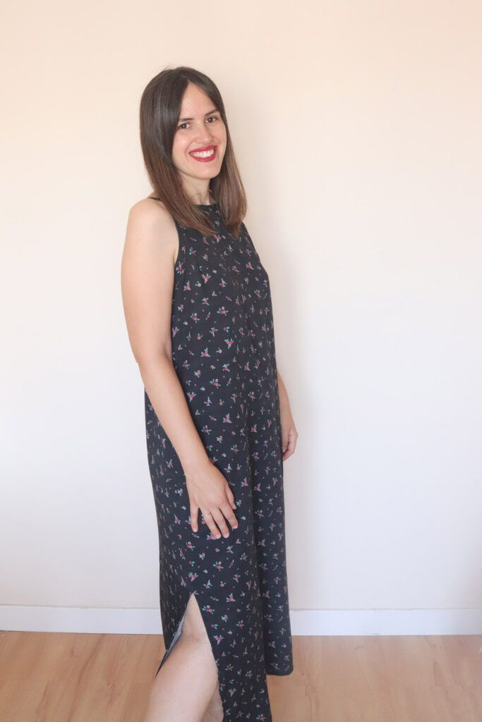 Mujer con melena castaña posa sonriente frente a la cámara, de medio perfil, con un vestido de tirantes, hasta casi los tobillos, confeccionado con la viscosa ecovero esencia floral negro de ODALOA.