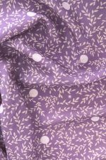 Tela, de aspecto fluido, de color morado orquídea con hojas color crema y topos blancos.