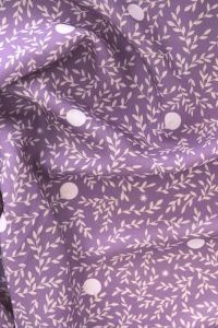 Tela, de aspecto fluido, de color morado orquídea con hojas color crema y topos blancos.