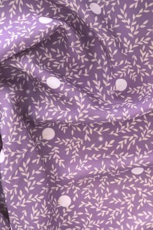 Tela, de aspecto fluido, de color morado orquídea con hojas color crema y topos blancos.