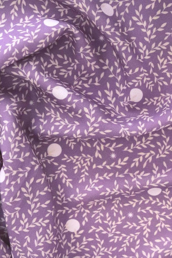 Tela, de aspecto fluido, de color morado orquídea con hojas color crema y topos blancos.