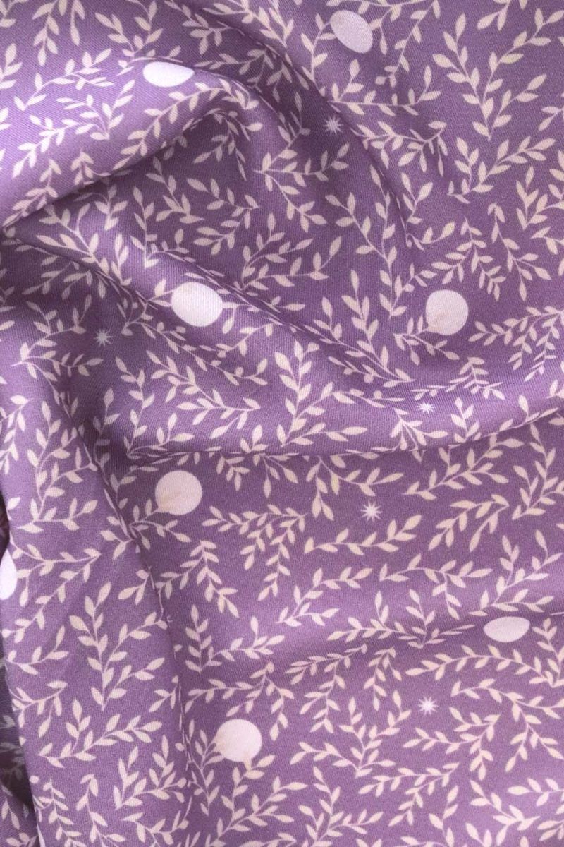 Tela, de aspecto fluido, de color morado orquídea con hojas color crema y topos blancos.