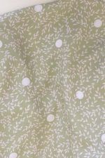 Tela, de aspecto fluido, de color verde claro con hojas color crema y topos blancos.