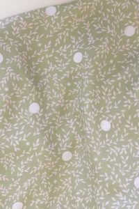 Tela, de aspecto fluido, de color verde claro con hojas color crema y topos blancos.