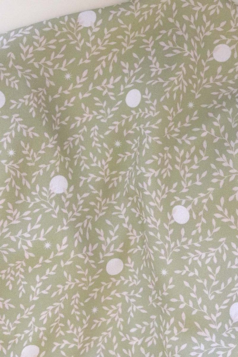 Tela, de aspecto fluido, de color verde claro con hojas color crema y topos blancos.