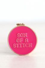 Needle_minder_son_of_a_stitch Porta agujas imantado. Tiene forma de bastidor de bordar redondo. Es de color fucsia y en el se puede leer "son of a stitch".