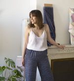 Mujer con amplia sonrisa y pelo castaño modela de perfil un diseño de pantalón con tela sostenible de color azul y patrones de líneas blancas que emulan el horizonte.