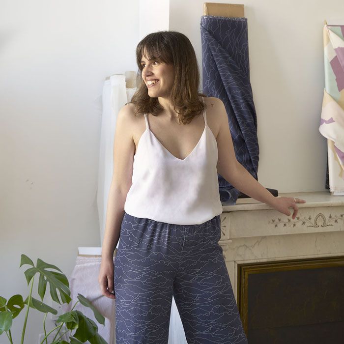 Mujer con amplia sonrisa y pelo castaño modela de perfil un diseño de pantalón con tela sostenible de color azul y patrones de líneas blancas que emulan el horizonte.
