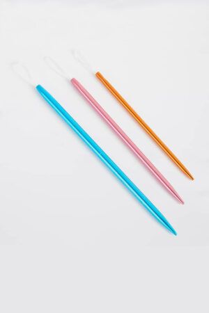 Tres agujas para lana sobre fondo gris. Cada una un poco más grande que la otra. Una aguja es azul, otra rosa y otra naranja.