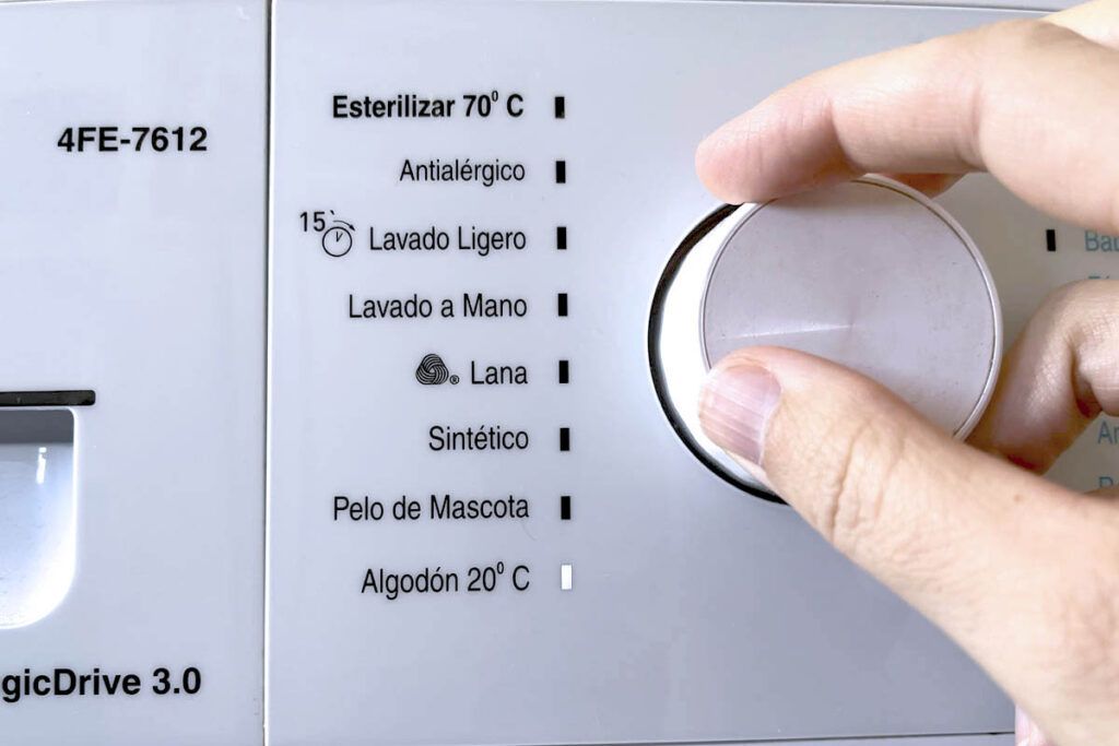 Imagen del cuadro de mandos de una lavadora blanca. Una mano de mujer gira el botón de selección. Se encuentra seleccionado el programa de lavado de algodón a 20ºC.