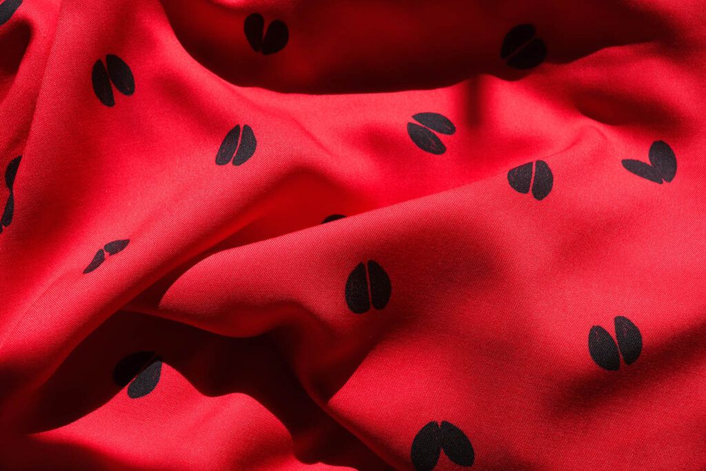 Tela de viscosa haciendo ondas, de color rojo intenso con motivos de huellas de ciervo en color azul oscuro casi negro.