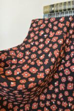 Una tela de fondo negro con flores que imitan las manchas de leopardo en color rojo coral y centro blanco cubre por completo un taburete. Sobre ella están, de manera horizontal dos libros antiguos de novelas en tonos verdes