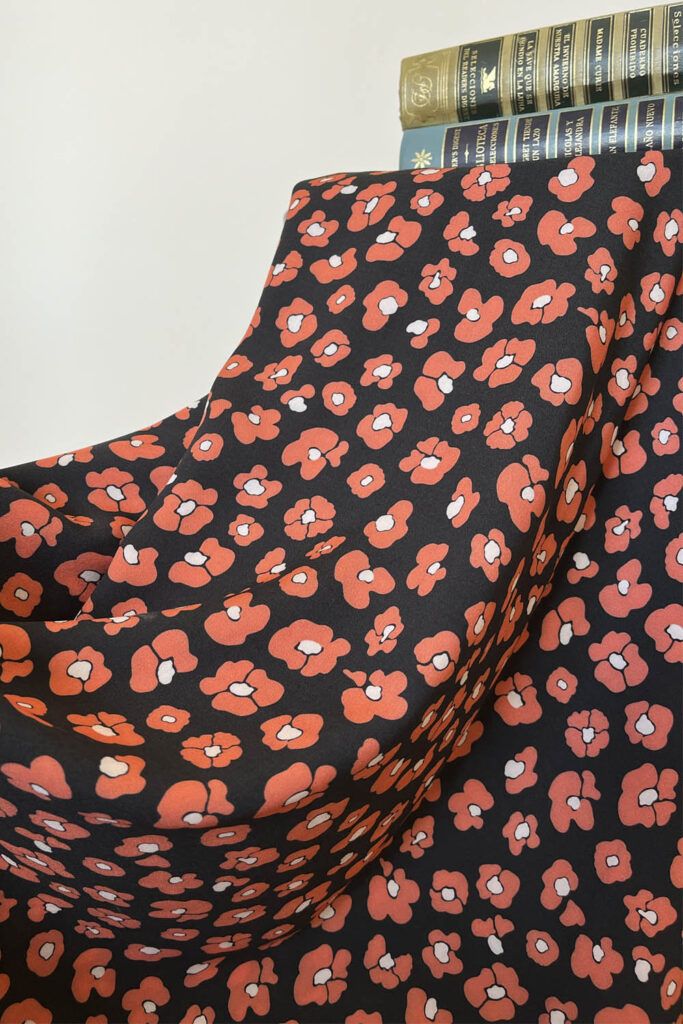 Una tela de fondo negro con flores que imitan las manchas de leopardo en color rojo coral y centro blanco cubre por completo un taburete. Sobre ella están, de manera horizontal dos libros antiguos de novelas en tonos verdes