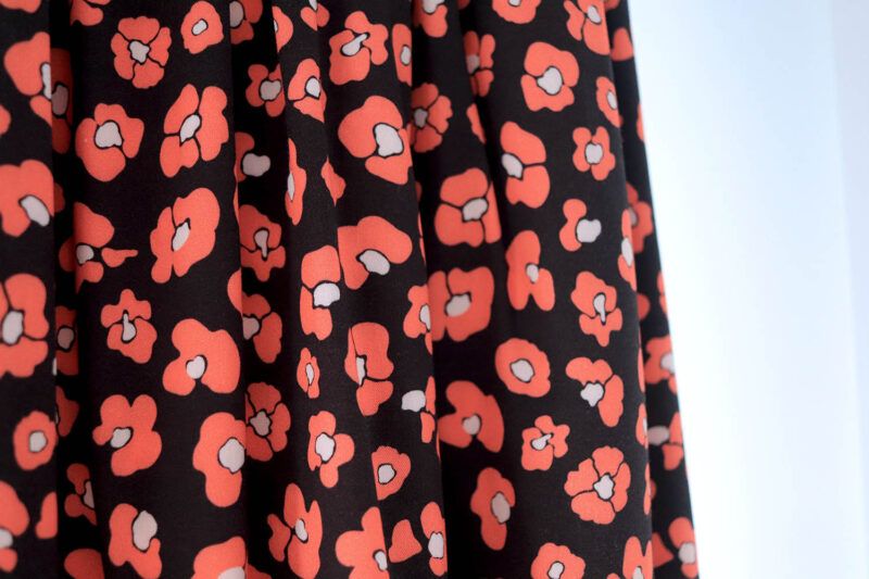 Una tela de fondo negro con flores que imitan las manchas de leopardo en color rojo coral y centro blanco.