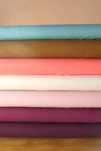 Tablillas de telas de punto camiseta de algodón orgánico en diferentes colores (aguamarina, aceituna, coral, natural, rosa palo, plum y mora) apiladas una encima de la otra