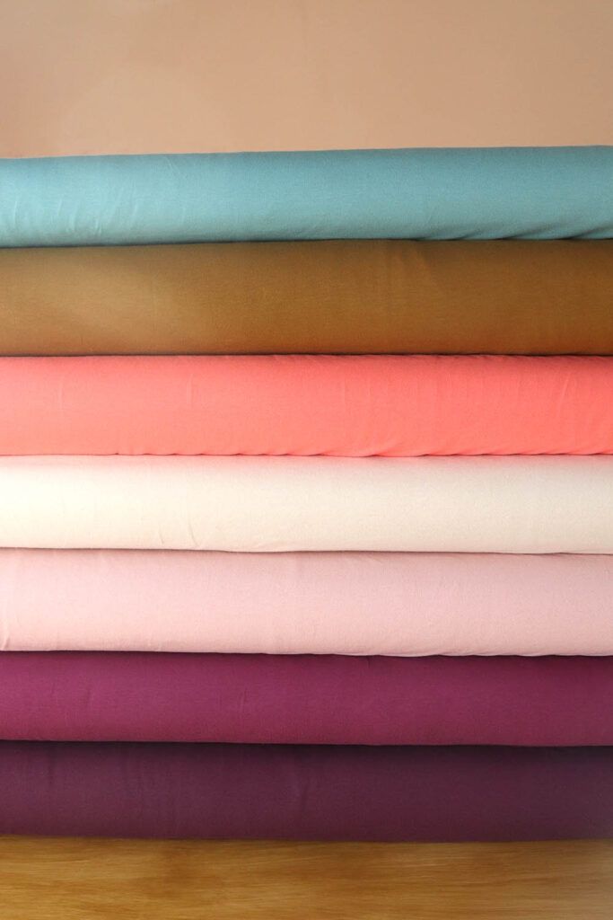Tablillas de telas de punto camiseta de algodón orgánico en diferentes colores (aguamarina, aceituna, coral, natural, rosa palo, plum y mora) apiladas una encima de la otra