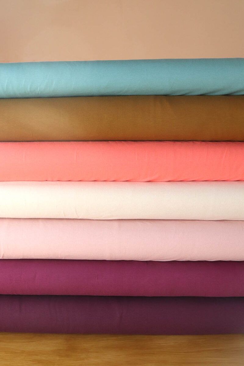 Tablillas de telas de punto camiseta de algodón orgánico en diferentes colores (aguamarina, aceituna, coral, natural, rosa palo, plum y mora) apiladas una encima de la otra
