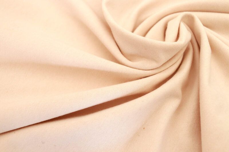 Plano cercano del entramado de una tela de punto jersey de algodón orgánico en su color natural. Se puede observar alguna semilla del algodón.