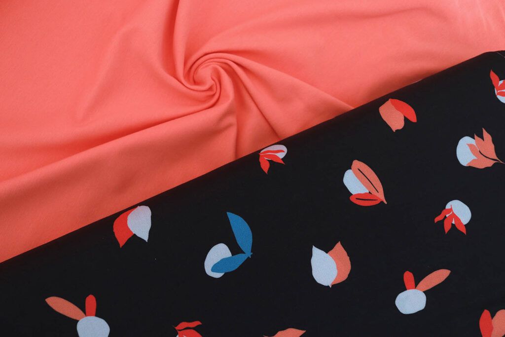 Imagen de dos telas que combinan entre sí. Una al lado de la otra. Una es una tela de punto camiseta en color coral y otra es una viscosa de color azul casi negro con pequeños motivos de piedras y hojas.