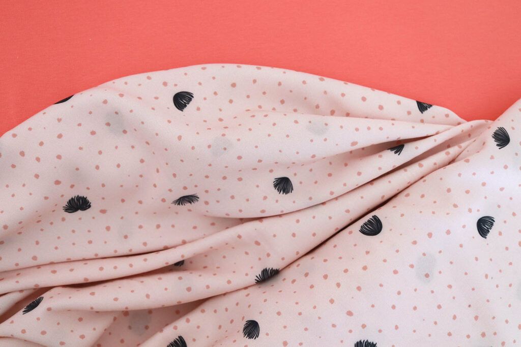Imagen de dos telas que combinan entre sí. Una al lado de la otra. Una es una tela de punto camiseta en color coral y otra es una viscosa de color en color salmón muy claro con puntitos en color salmón más fuerte y pequeñas flores en color azul marino.