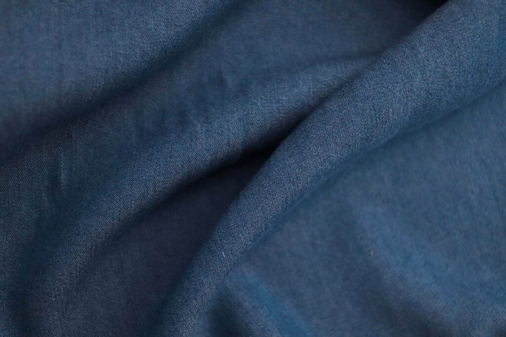 Primerísmo plano de una tela de Tencel con acabado denim azul oscuro. La tela no está completamente estirada, si no que hace surcos mostrando el comportamiento de una tela con caída.