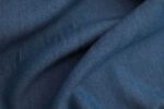 Tela Tencel Denim Primerísmo plano de una tela de Tencel con acabado denim azul oscuro. La tela no está completamente estirada, si no que hace surcos mostrando el comportamiento de una tela con caída.