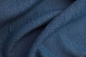 Primerísmo plano de una tela de Tencel con acabado denim azul oscuro. La tela no está completamente estirada, si no que hace surcos mostrando el comportamiento de una tela con caída.