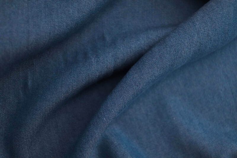 Primerísmo plano de una tela de Tencel con acabado denim azul oscuro. La tela no está completamente estirada, si no que hace surcos mostrando el comportamiento de una tela con caída.