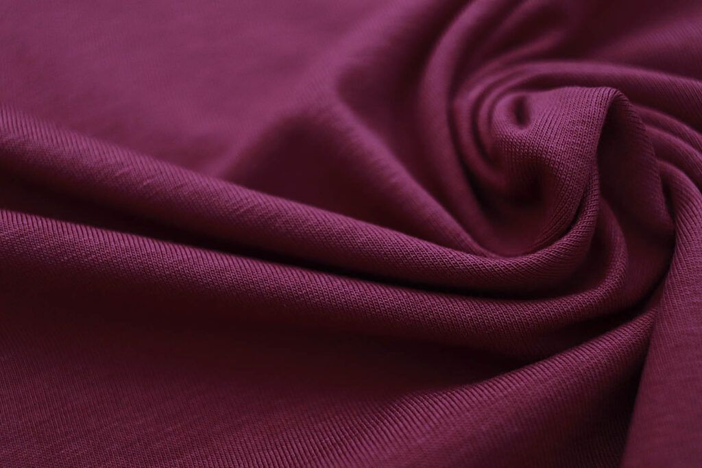 Plano cerca de la textura de una tela de punto camiseta de algodón orgánico en color ciruela plum