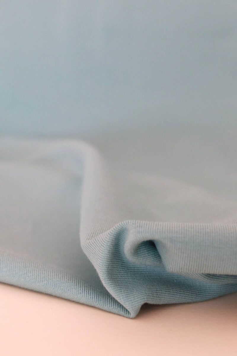 Plano cercano de la textura de una tela de punto jersey de algodón orgánico en color aguamarina.