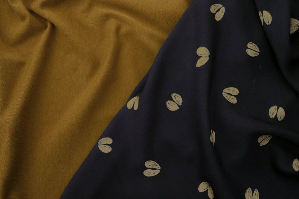 Combinación de tela punto jersey de algodón orgánico con viscosa azul oscuro con motivo de huellas de ciervo. Ambas están puestas, de manera fluida, generando pliegues, la una al lado de la otra.