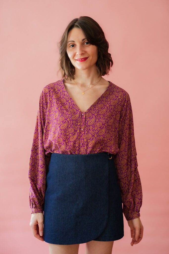Mujer de pelo castaño y delicada sonrisa que armoniza un diseño de Falda y pantalón Charlie Apolline Patterns en fondo pastel.
