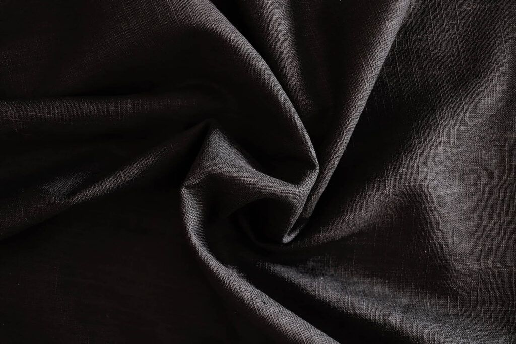 Detalle de una tela de ramio negro, de aspecto como el lino. Se han hecho unos pliegues en el centro con forma de espiral.
