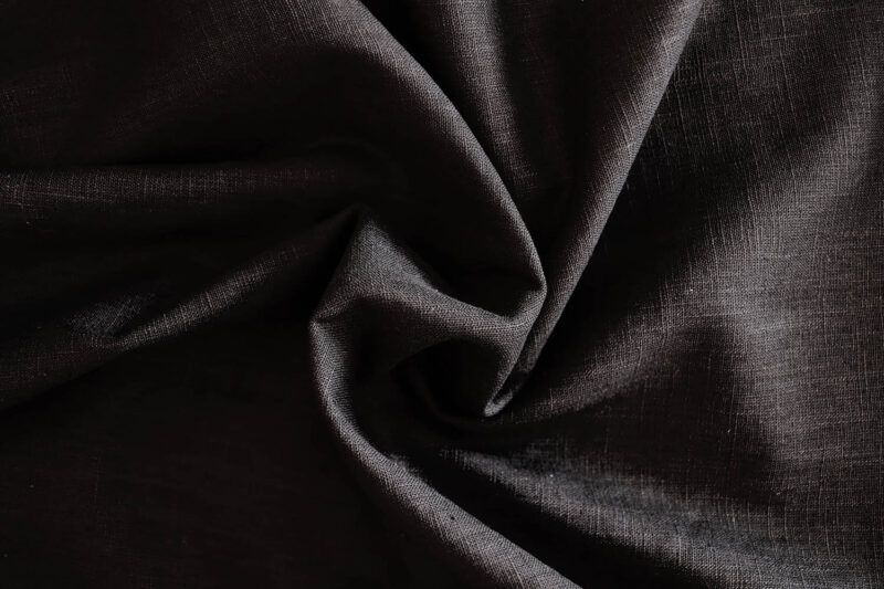 Detalle de una tela de ramio negro, de aspecto como el lino. Se han hecho unos pliegues en el centro con forma de espiral.