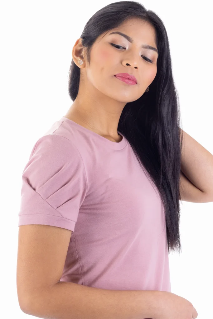 Plano medio de una chica asiática, de pelo largo moreno. Se encuentra de perfil y lleva una camiseta de manga corta con mangas con pliegues en color rosa.
