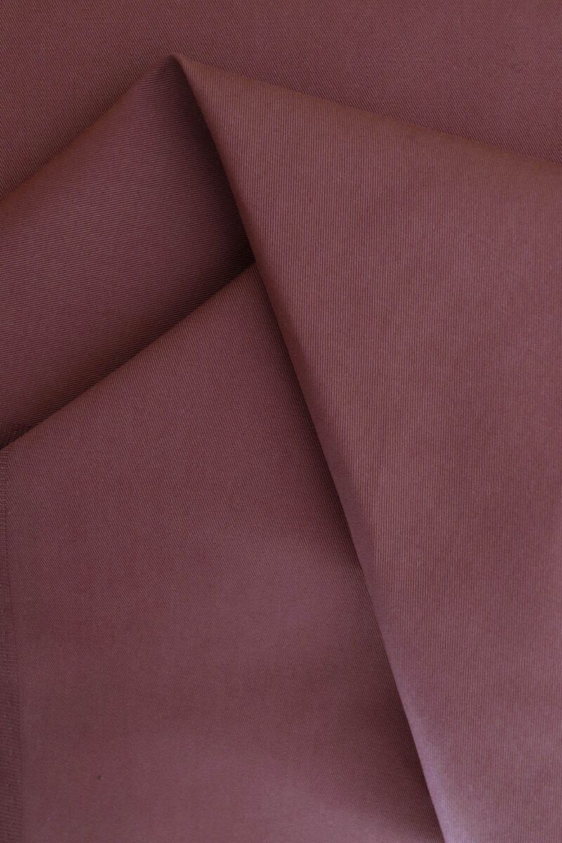 Tela de gabardina rosa terracota que hace unos pliegues sobre sí misma.