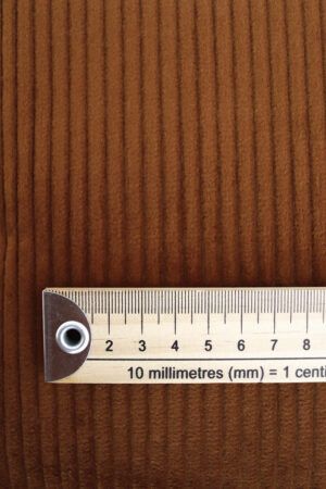 Plano cercano de una tela de pana marrón. Encima de ella se encuentra una regla de madera que indica el tamaño de los bordones, aproximadamente de 5 mm cada uno.