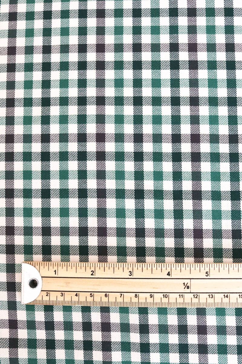 Tela de sarga de algodón de cuadros en distintos tono de verde y crudo. Sobre ella hay una regla de madera, mostrando así el tamaño del cuadro, que es aproximadamente de medio centímetro.
