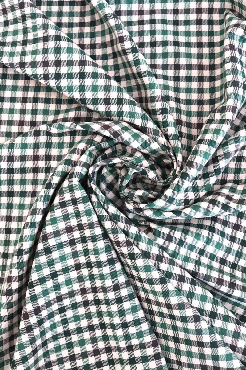 Tela de sarga de algodón de cuadros en distintos tono de verde y crudo. La tela hace dobleces en forma de círculo.