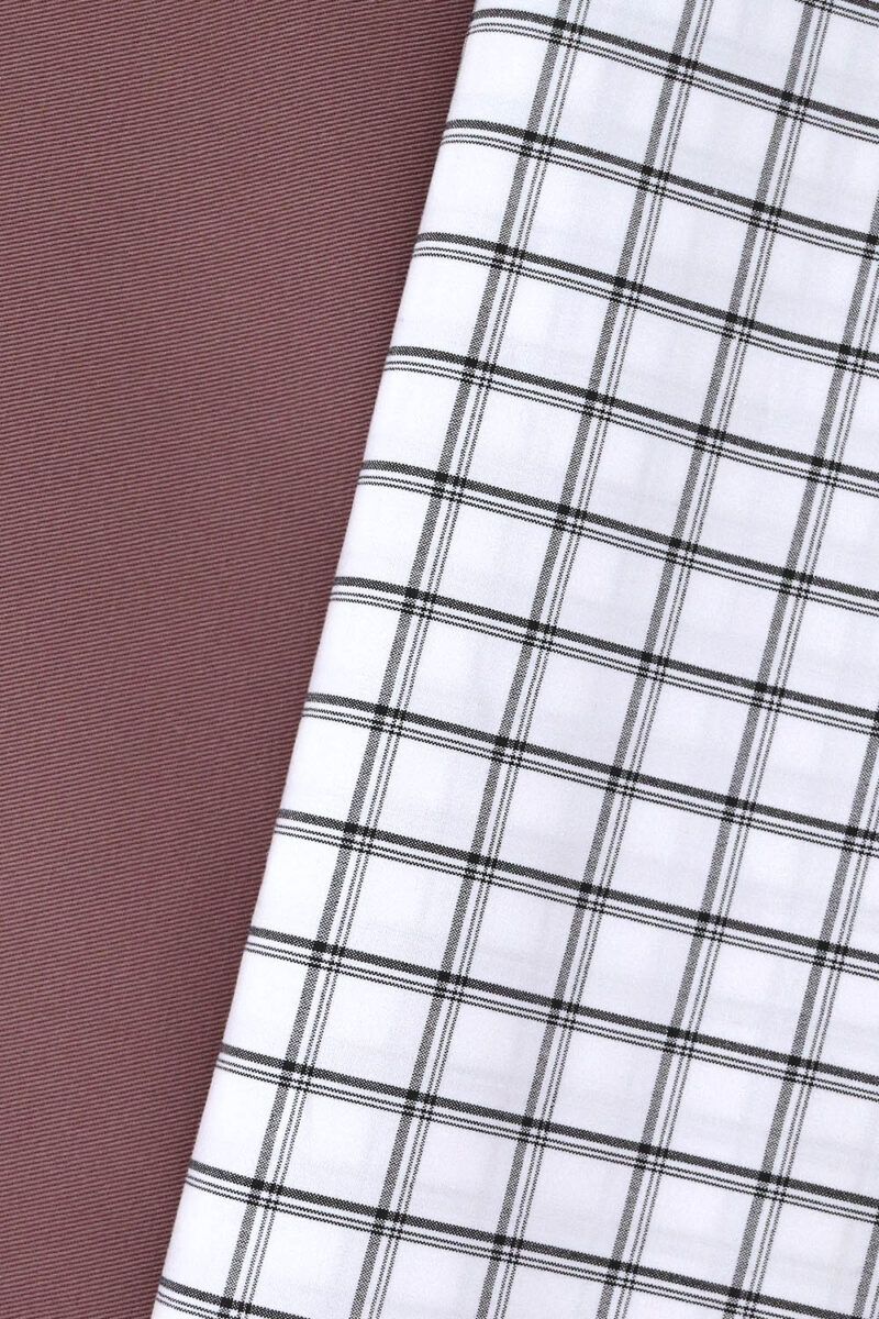 Tela de cuadros blanco y negro y gabardina Tela blanca con rayas horizontales y verticales, de diferentes grosores, en color negro, formando cuadros. La tela se encuentra sobre otra de gabardina en color rosa.