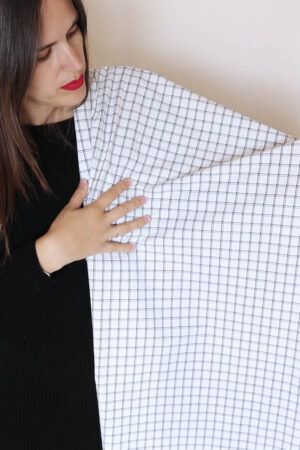 Una chica vestida de negro y con pelo largo, castaño sostiene sobre su hombro, mientras la mira, una tela de cuadros blanco y negro.