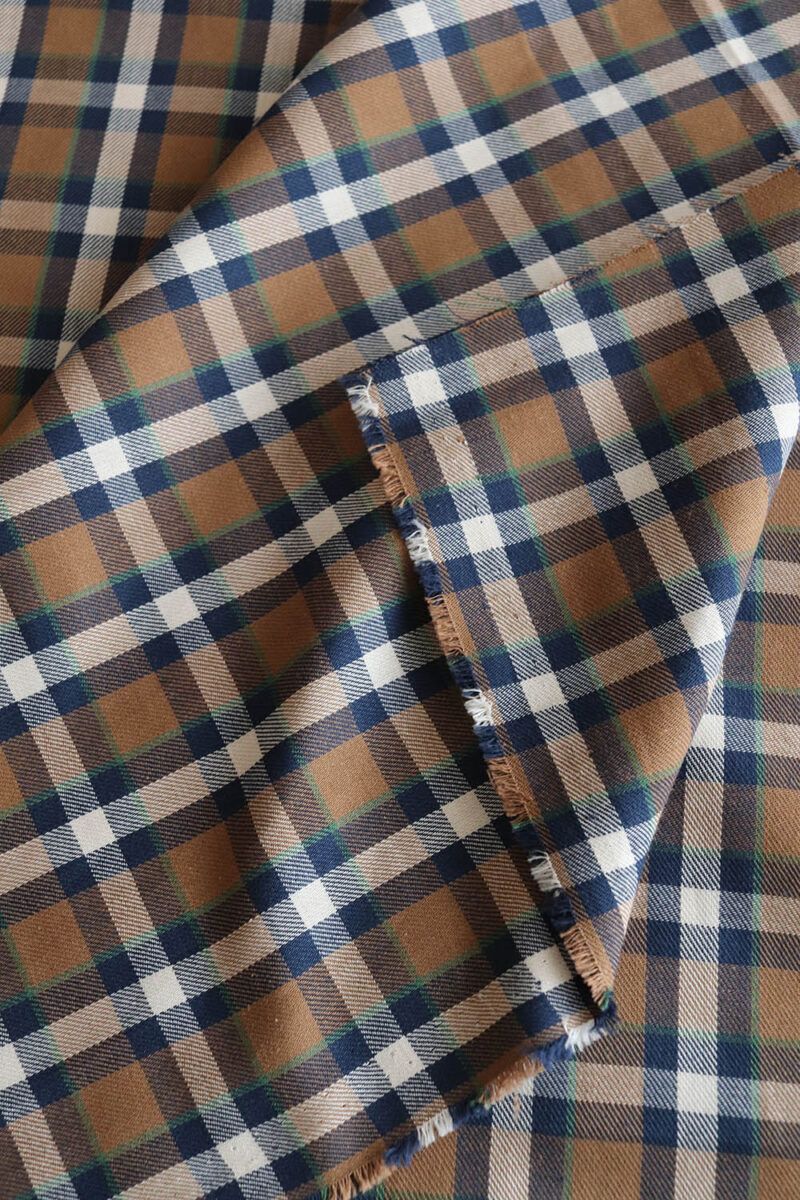 Tela de cuadros en tonos marrón, azul, verde y crudo. La tela está doblada sobre uno de sus lados para mostrar tanto el derecho como el revés de la tela.