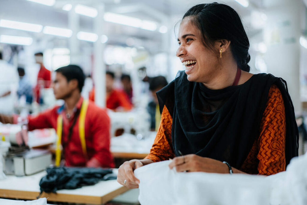 Mujer india, de pelo moreno y recogido, se ríe mientras trabaja en un fábrica textil certificada GOTS, una de las alternativas al algodón convencional