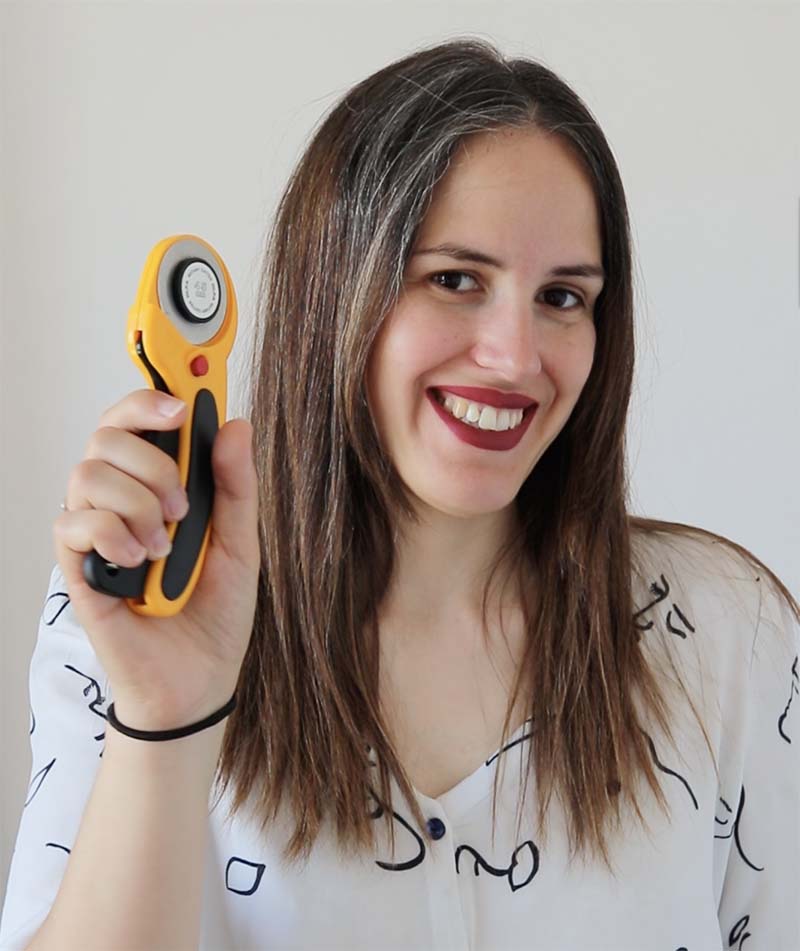 Mujer con pelo largo y castaño sonríe mientras sujeta con una mano un cúter rotatorio de color amarillo y negro