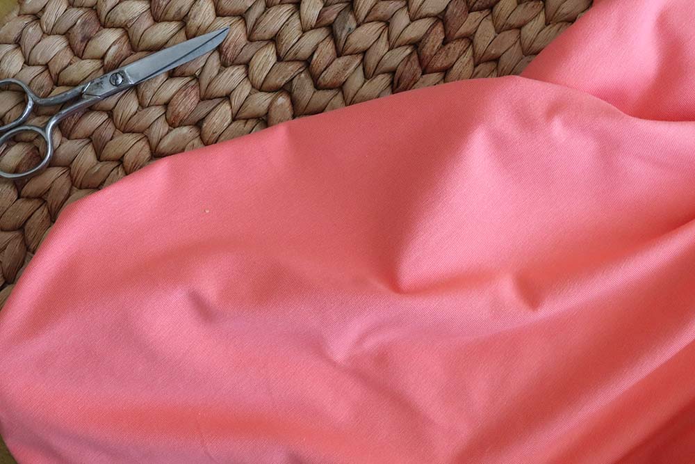 Tela de punto jersey de algodón orgánico en color coral, a su lado hay unas tijeras de costura metálicas