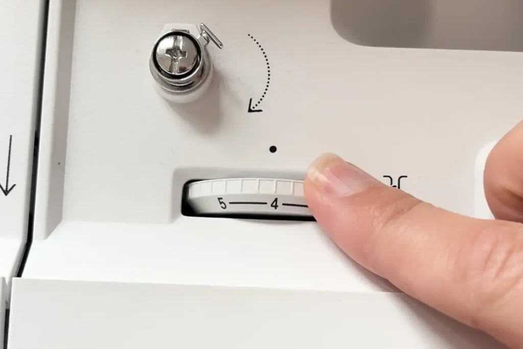 Un dedo selecciona el nivel de tensión 4 en el dial de una máquina de coser blanca.