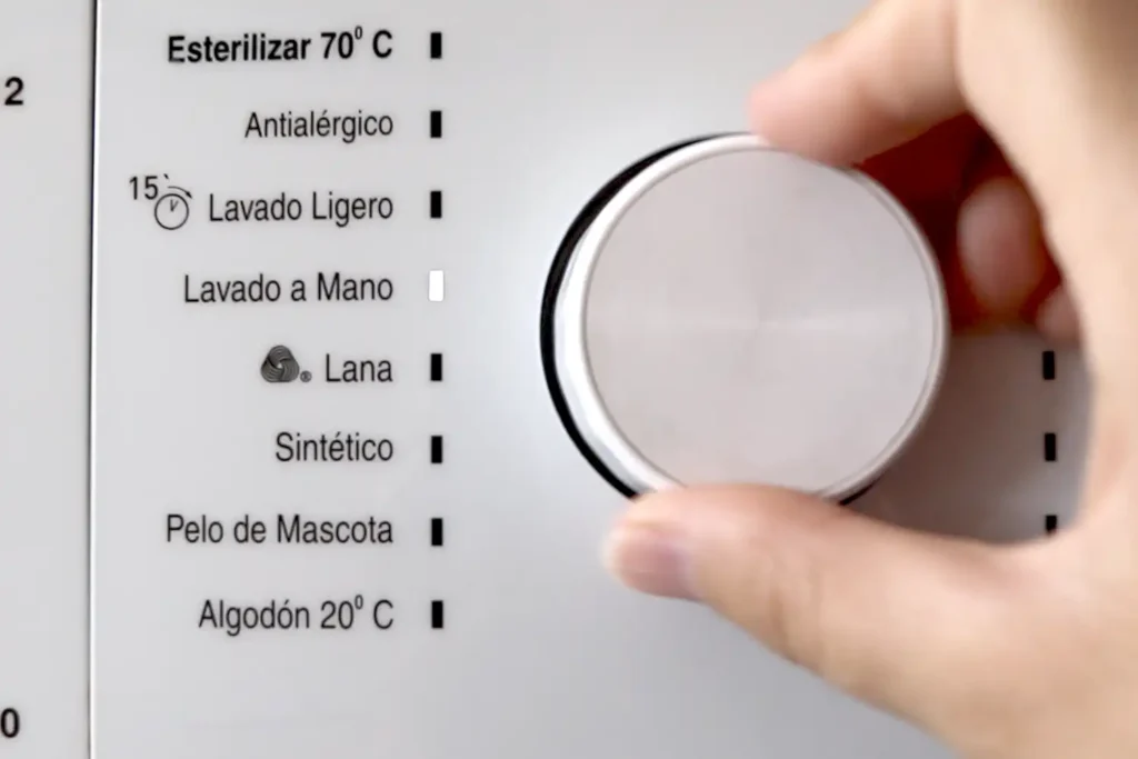 Mano seleccionando el programa de lavado a mano en el panel de una lavadora para lavar prendas de viscosa.