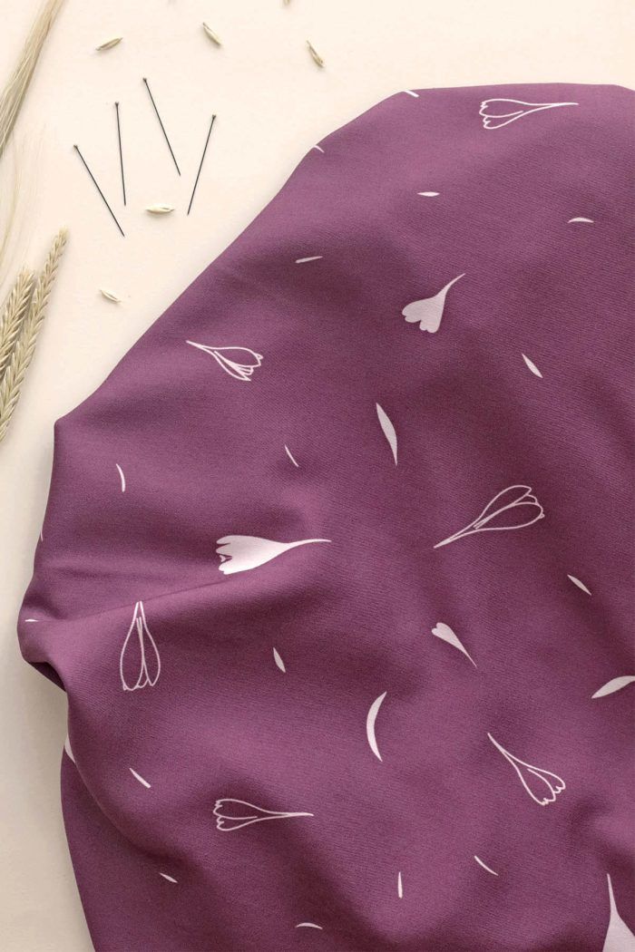 Tela de viscosa EcoVero de color ciruela con motivos de flores y hojas en color blanco con tintes ciruela.